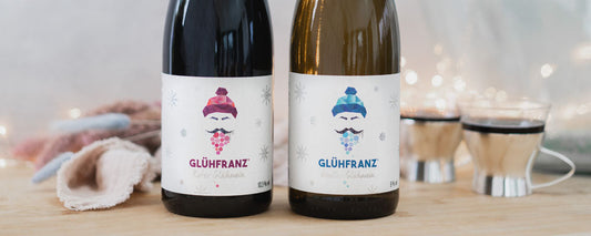 Glühfranz roter und weißer Glühwein mit Tassen und Lichtern im Hintergrund