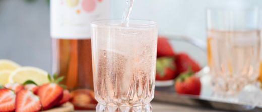 Glas Weinschorle mit Früchten und Roséweinflasche im Hintergrund